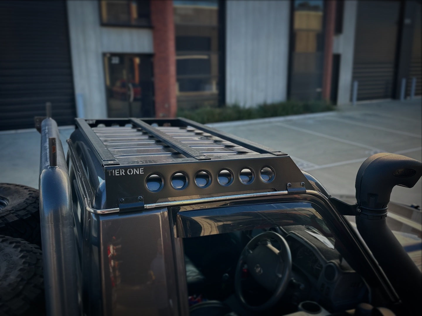 This is an image of a black Tier One Metalworks roof rack and rails mounted on a dark 4x4 vehicle with a snorkel