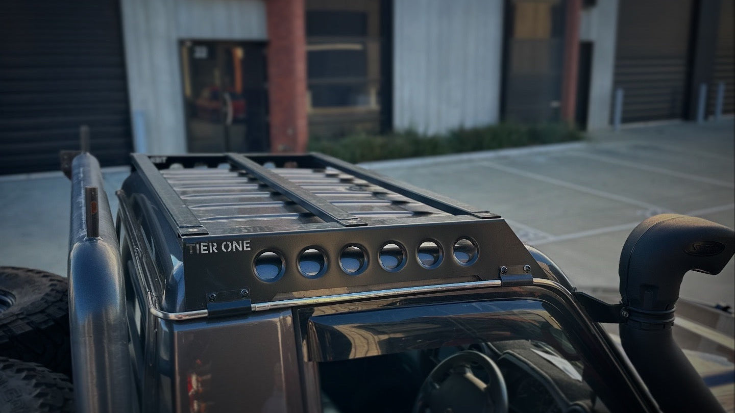 This is an image of a black Tier One Metalworks roof rack and rails mounted on a dark 4x4 vehicle with a snorkel