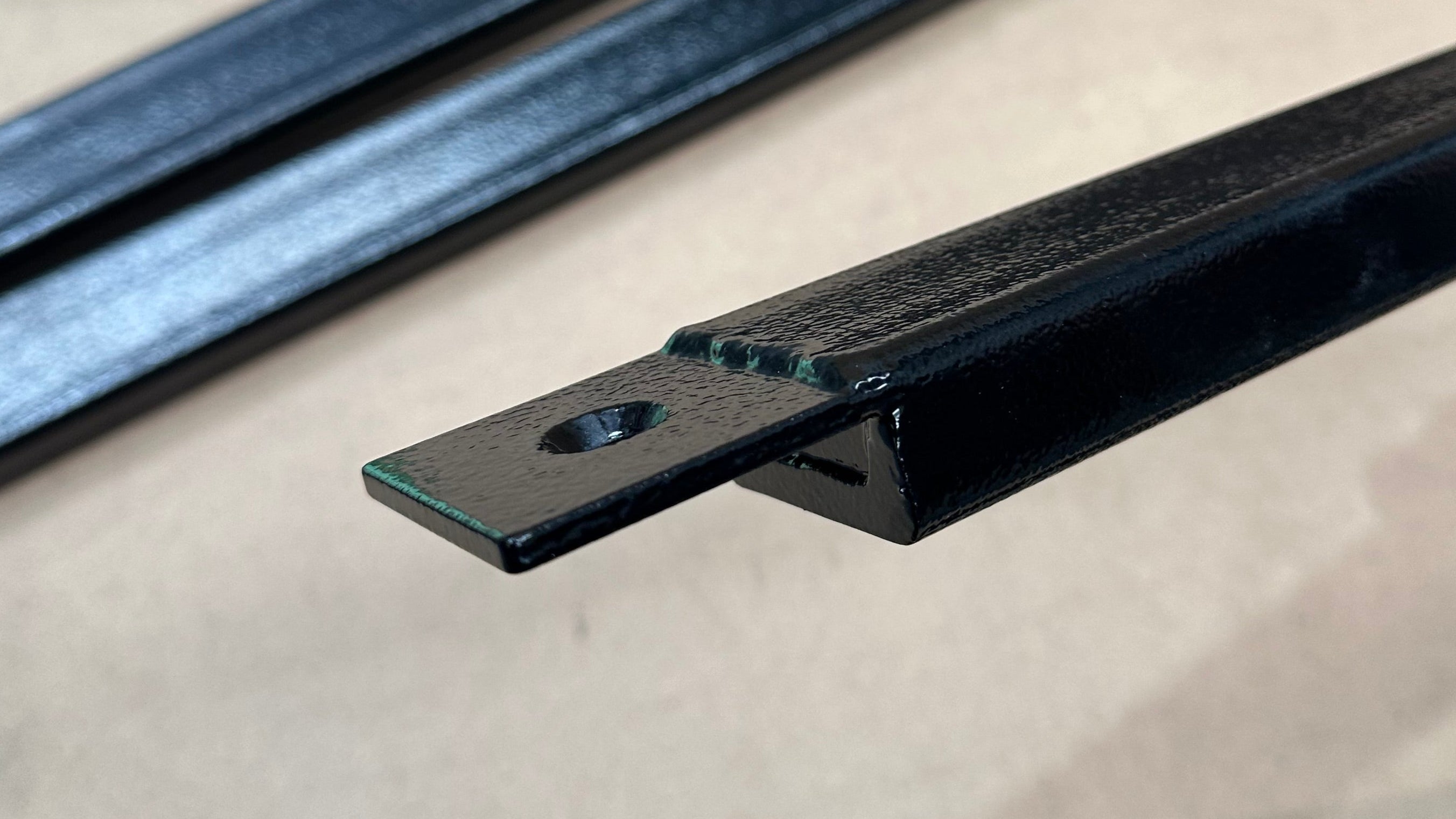 This is an image of a close-up of a black metal roof rack rail component by Tier One Metalworks