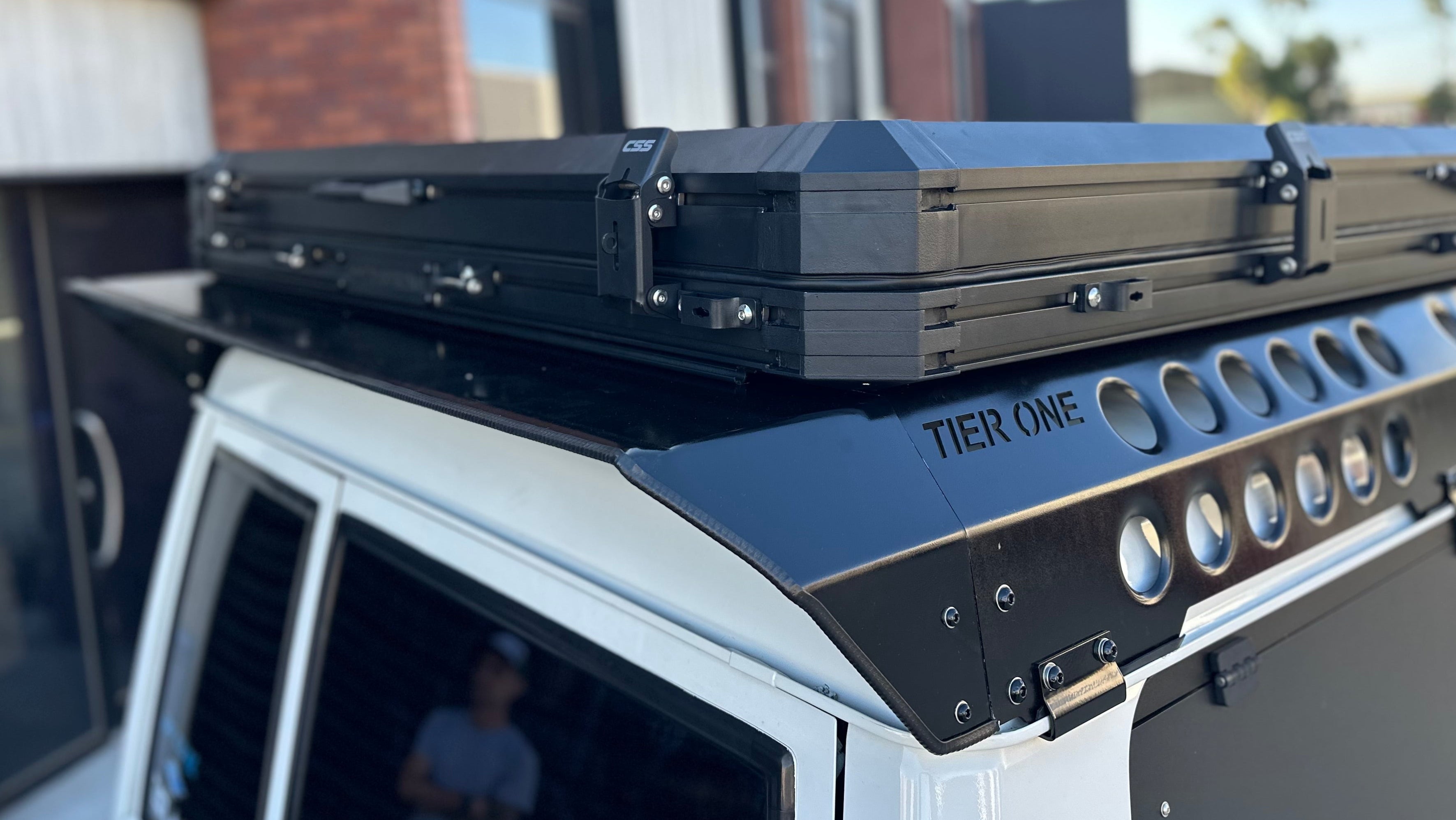 This is an image of Tier One Metalworks black roof rack and rails mounted on a white 4x4 vehicle with CSS rooftop tent