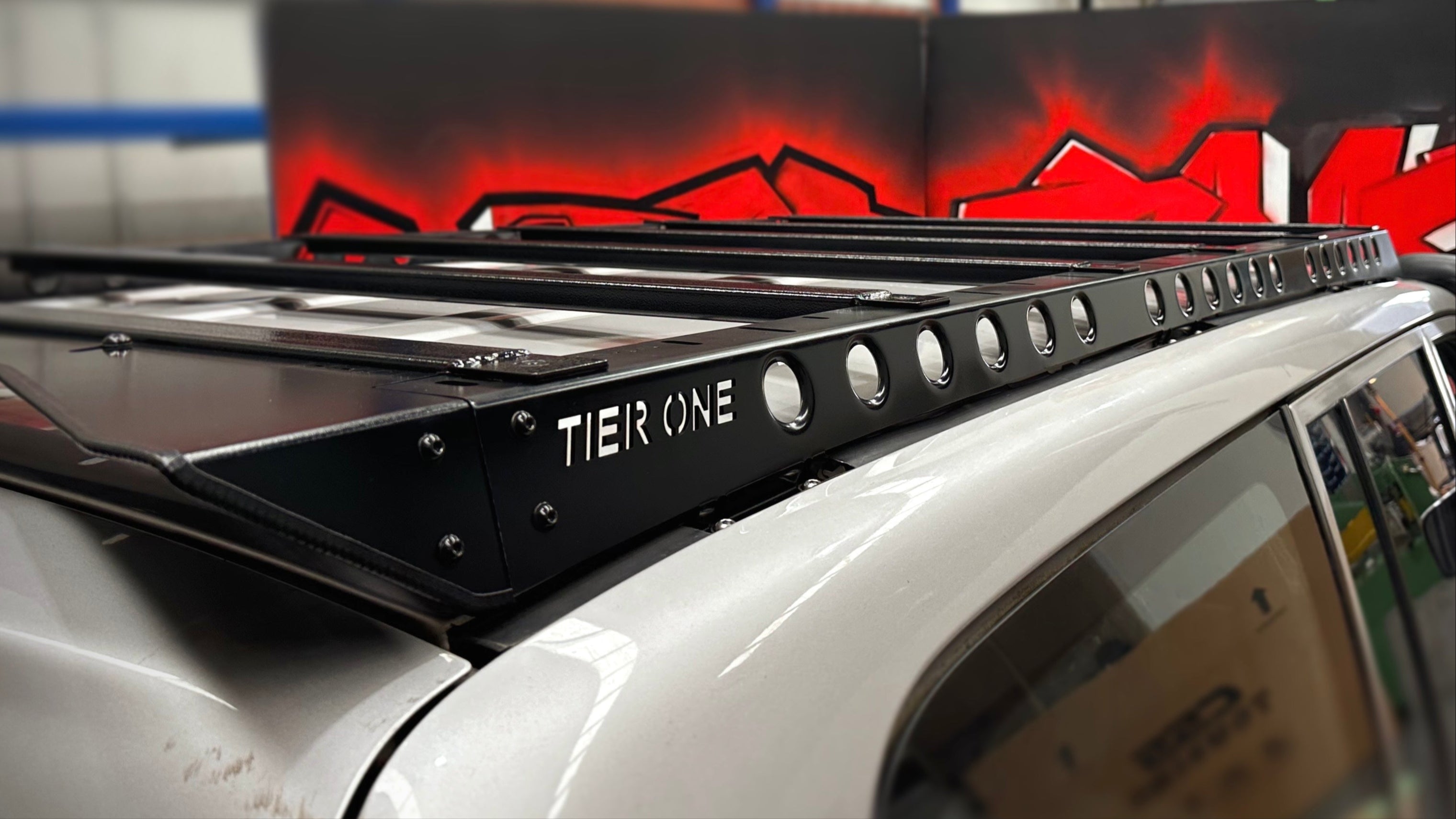 This is an image of a black Tier One Metalworks Roof Rack installed on a white 4x4 vehicle inside a workshop