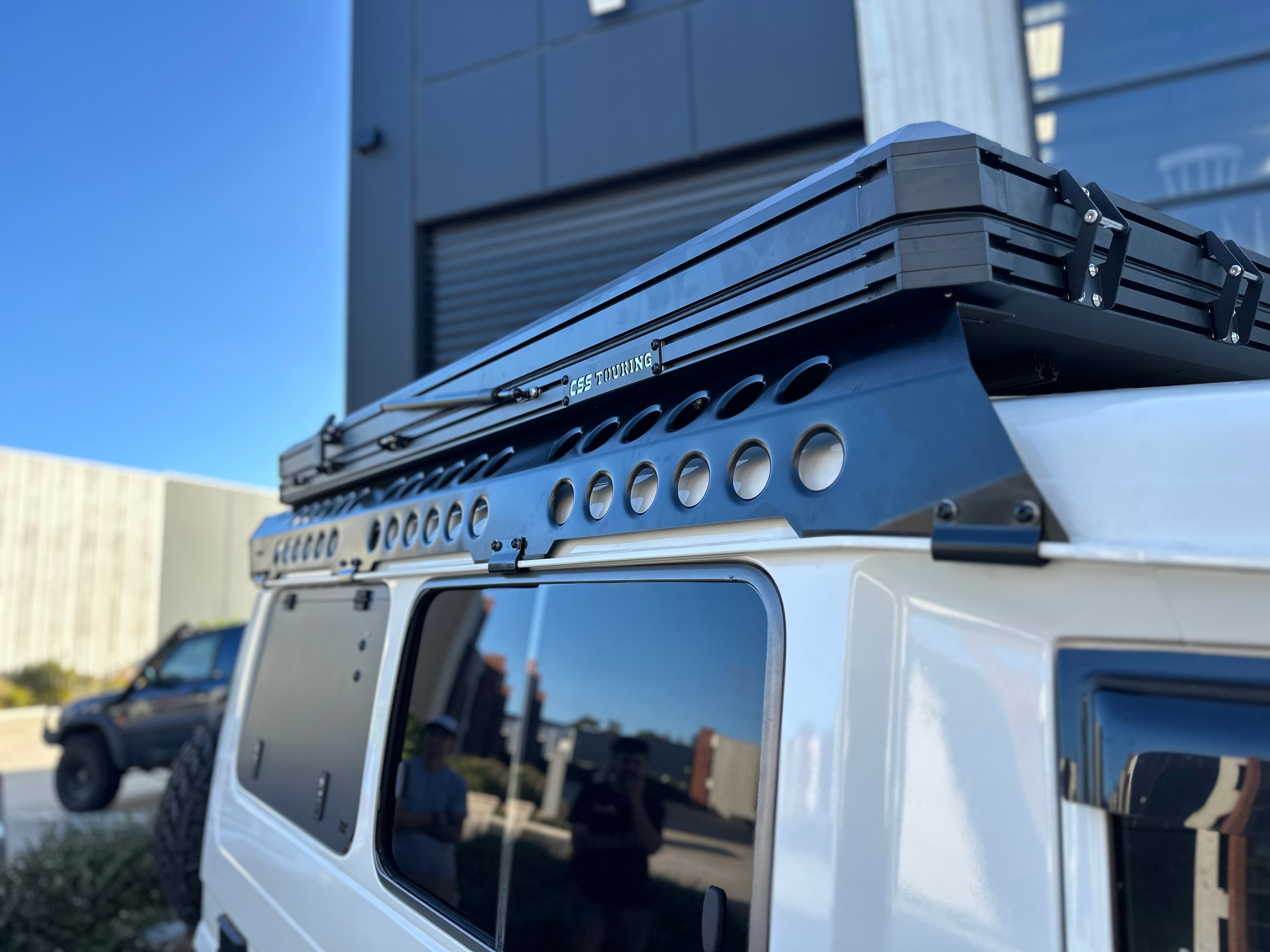 This is an image of a white 4x4 with a black CSS Touring rooftop tent on Tier One Metalworks roof racks and rails