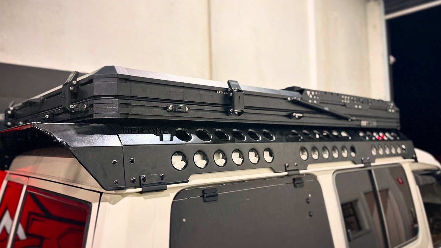 This is an image of a white 4x4 vehicle with a Tier One Metalworks black roof rack and rails fitted, photographed indoors.