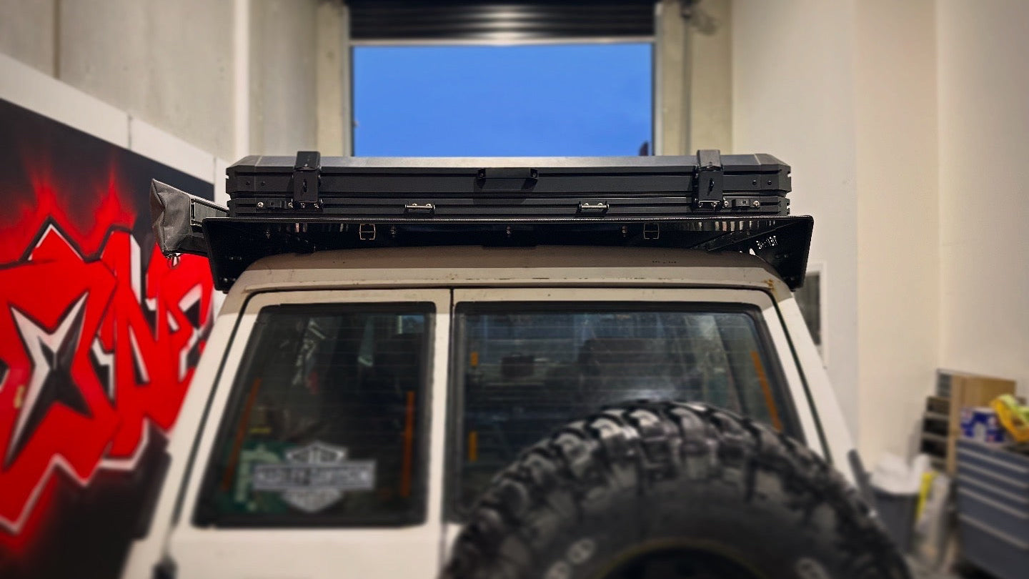 This is an image of a white 4x4 vehicle with Tier One Metalworks Roof Racks installed, parked inside a garage.