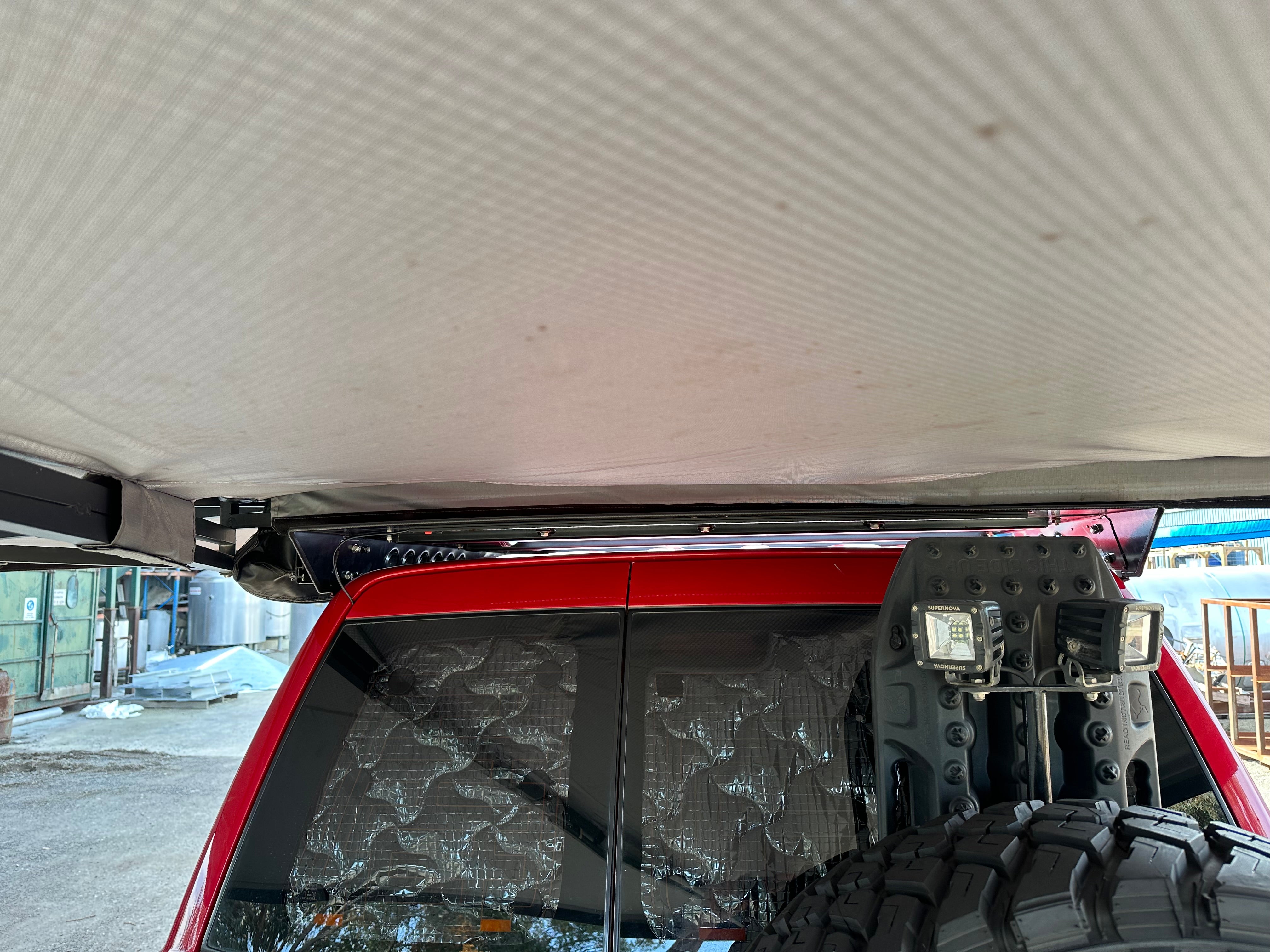 This is an image of a red 4x4 with a Tier One Metalworks roof rack supporting an extended awning in a workshop setting