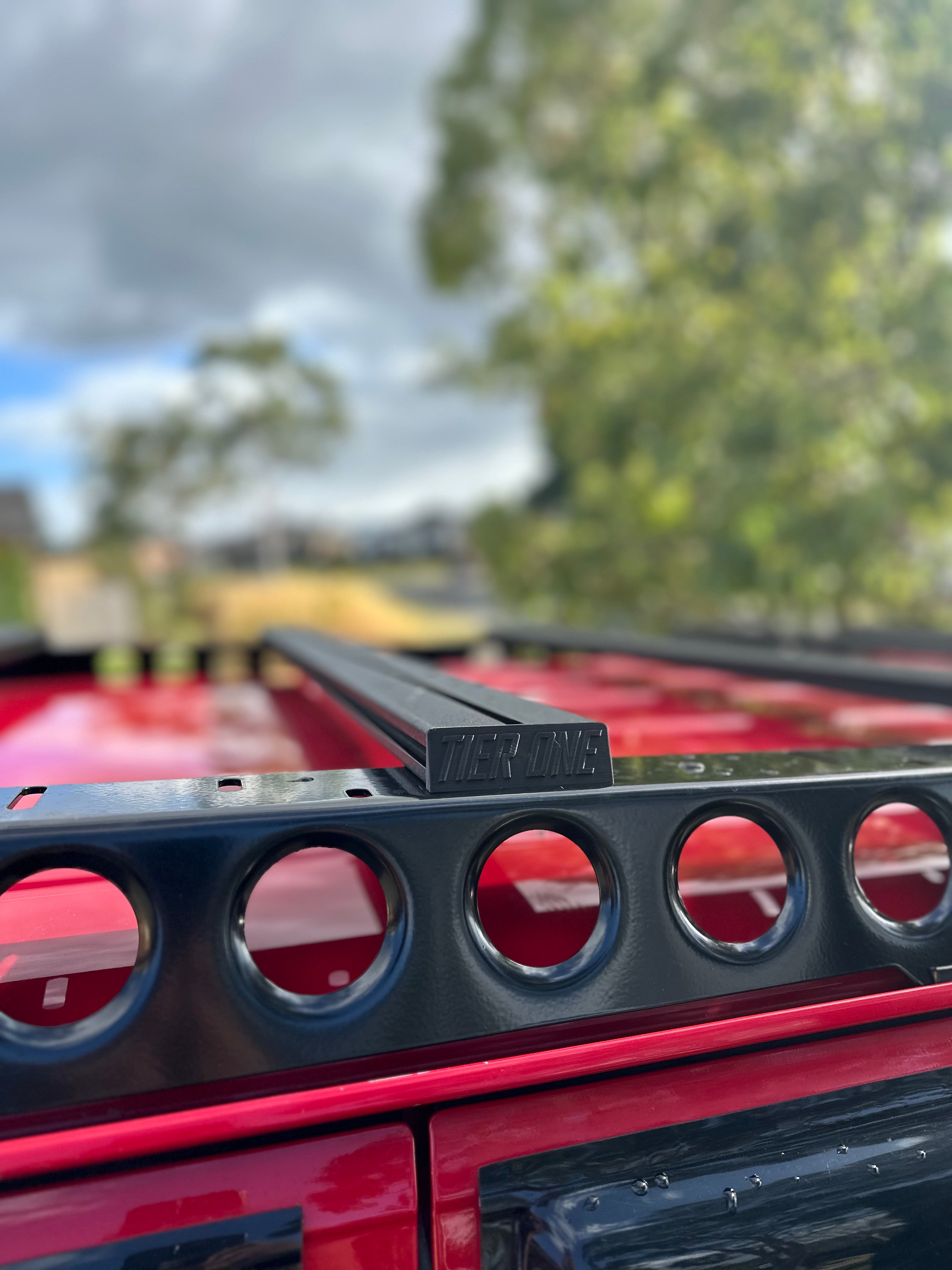 This is an image of a black Tier One Metalworks roof rack mounted on a red vehicle under a partly cloudy sky
