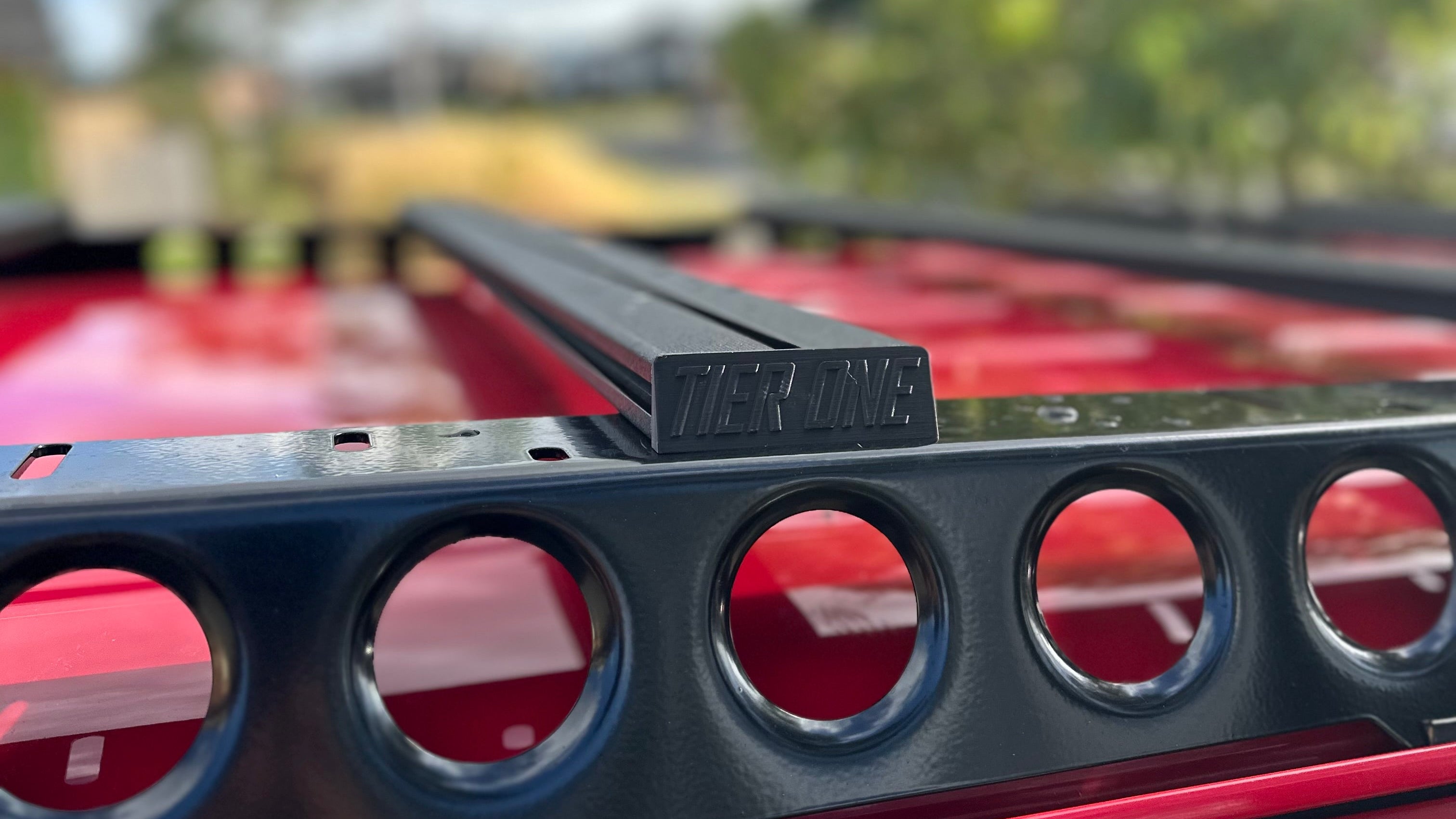 This is an image of a black Tier One Metalworks roof rack mounted on a red vehicle under a partly cloudy sky