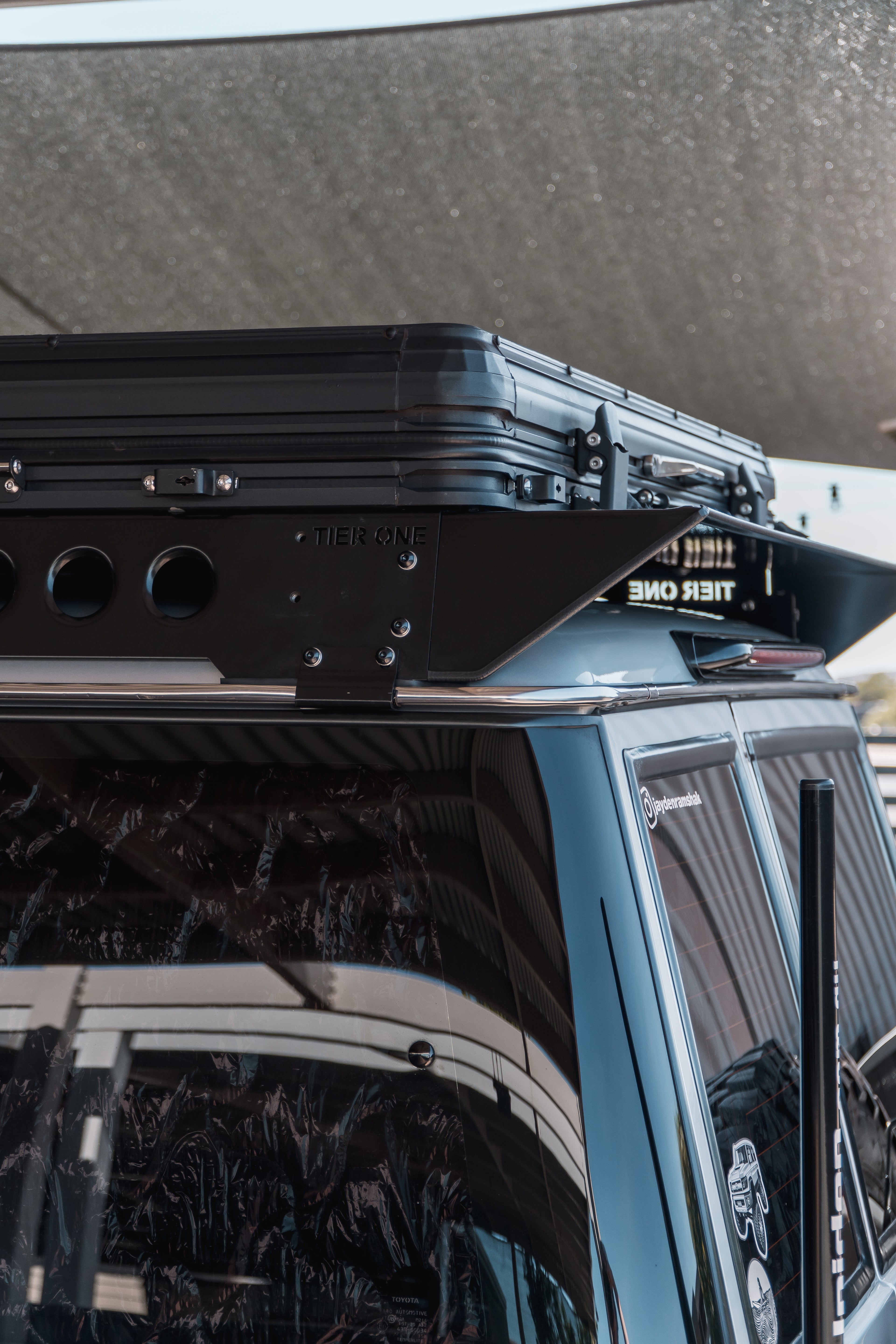 This is an image of a black Tier One Metalworks Roof Rack on a blue 4WD vehicle under shade