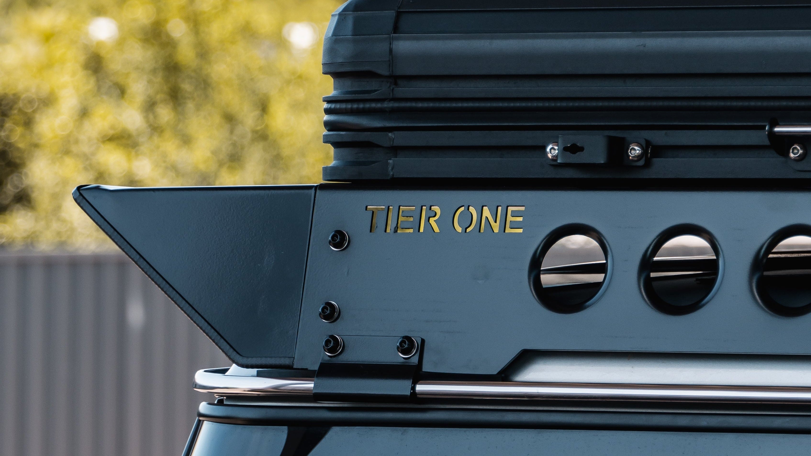 This is an image of a Tier One Metalworks black roof rack on a 4x4 vehicle with yellow background trees