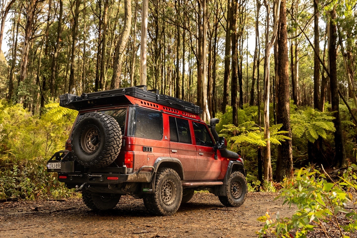 This is an image of a red Nissan Patrol 4WD with Tier One Metalworks roof racks and rails, off-road tyres, and snorkel in a dense Australian bush setting