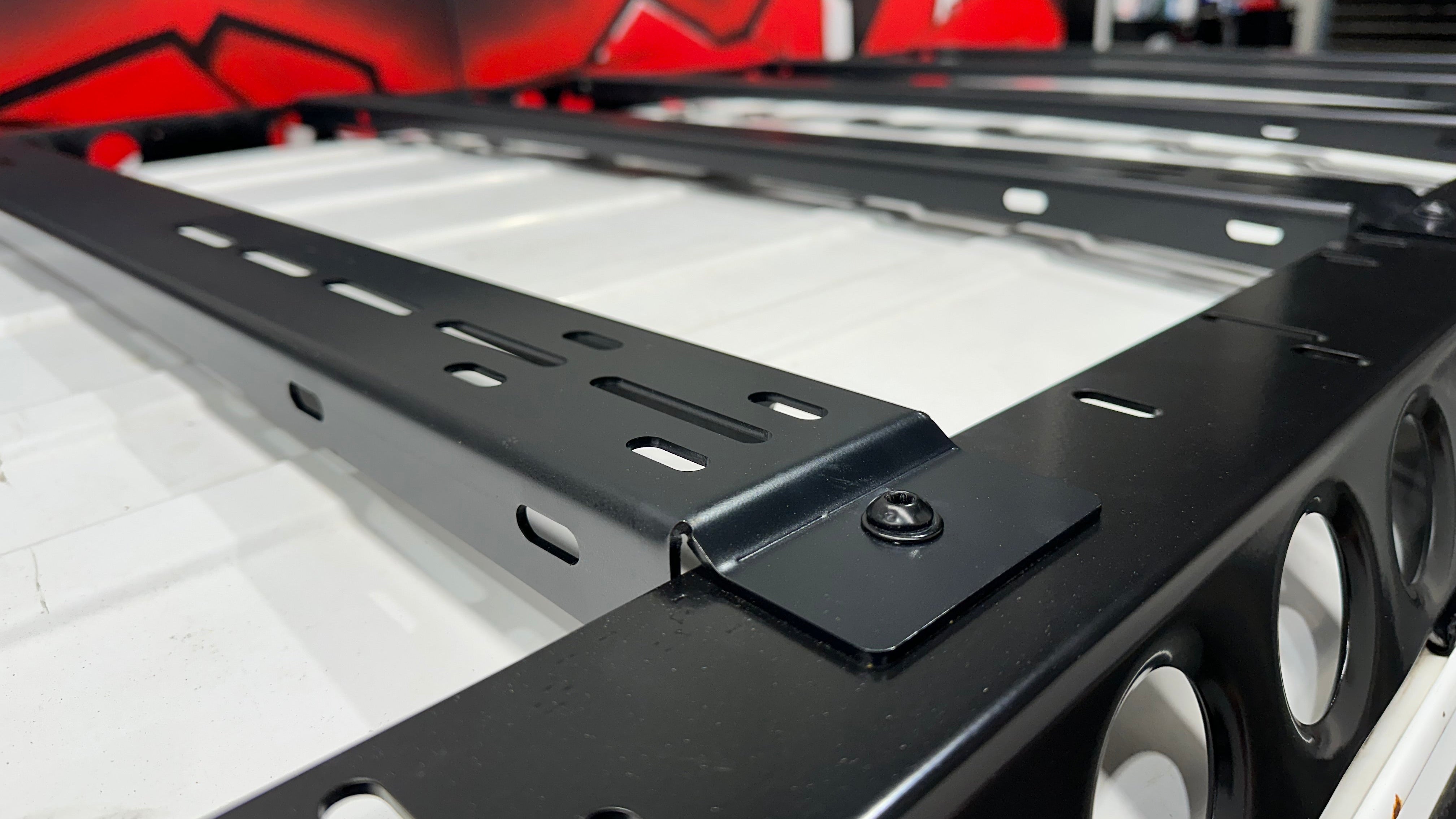 This is an image of a black Tier One Metalworks roof rack with multiple mounting slots on a white vehicle roof inside a workshop