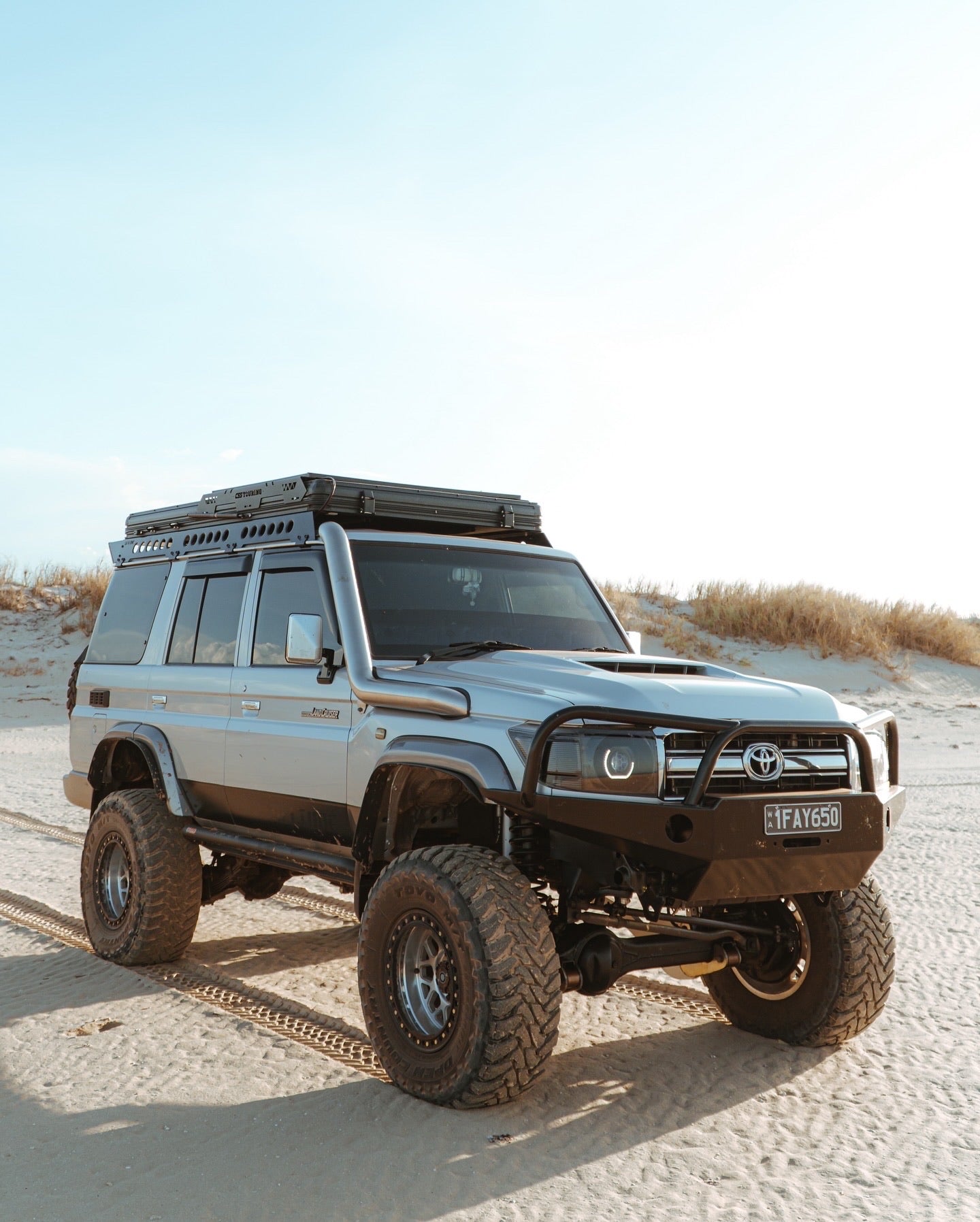 This is an image of a silver Toyota Land Cruiser 4x4 with Tier One Metalworks roof rack and snorkel on sandy terrain