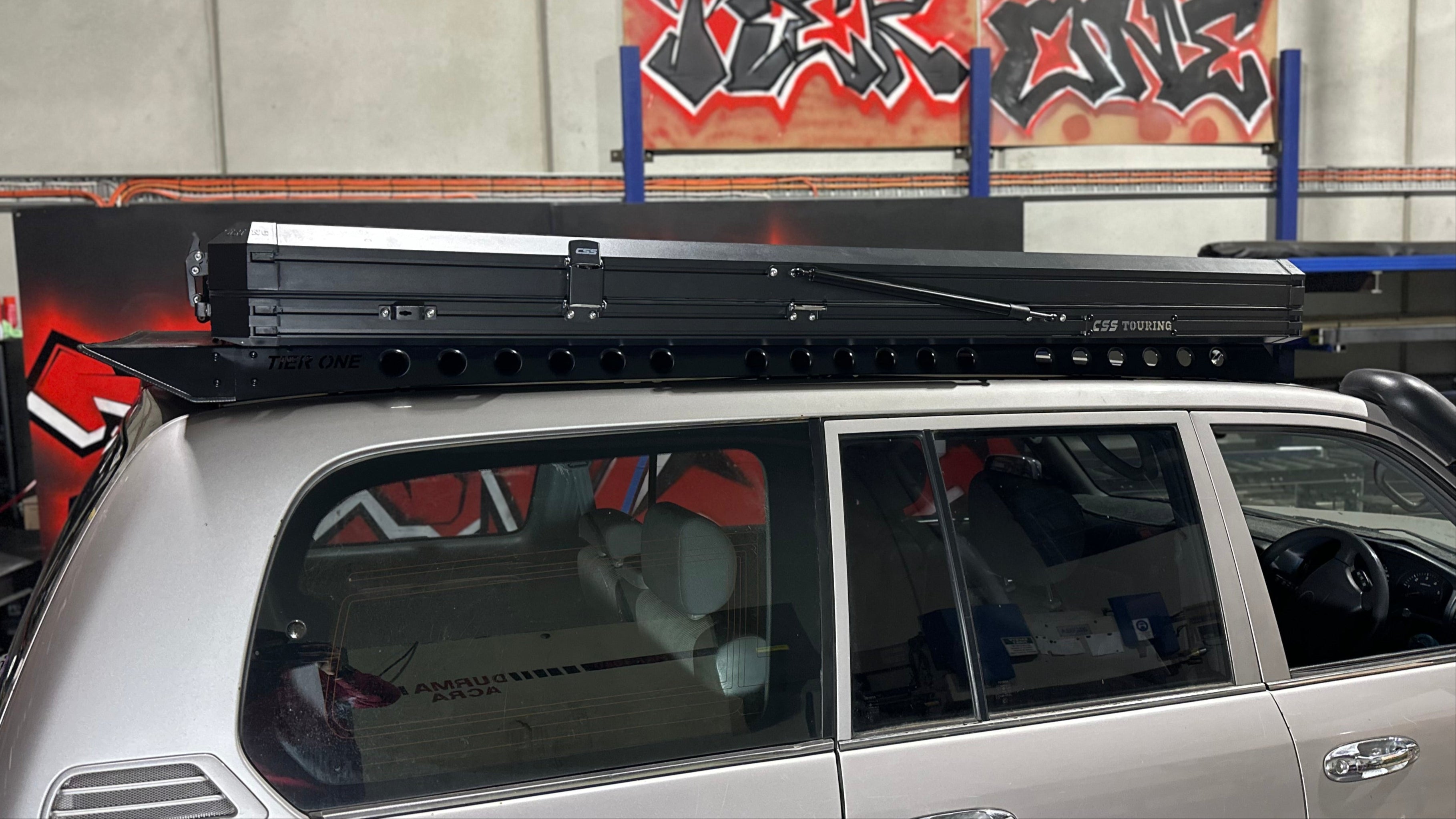 This is an image of a silver 4x4 with Tier One Metalworks roof racks and a CSS Touring rooftop tent mounted on top