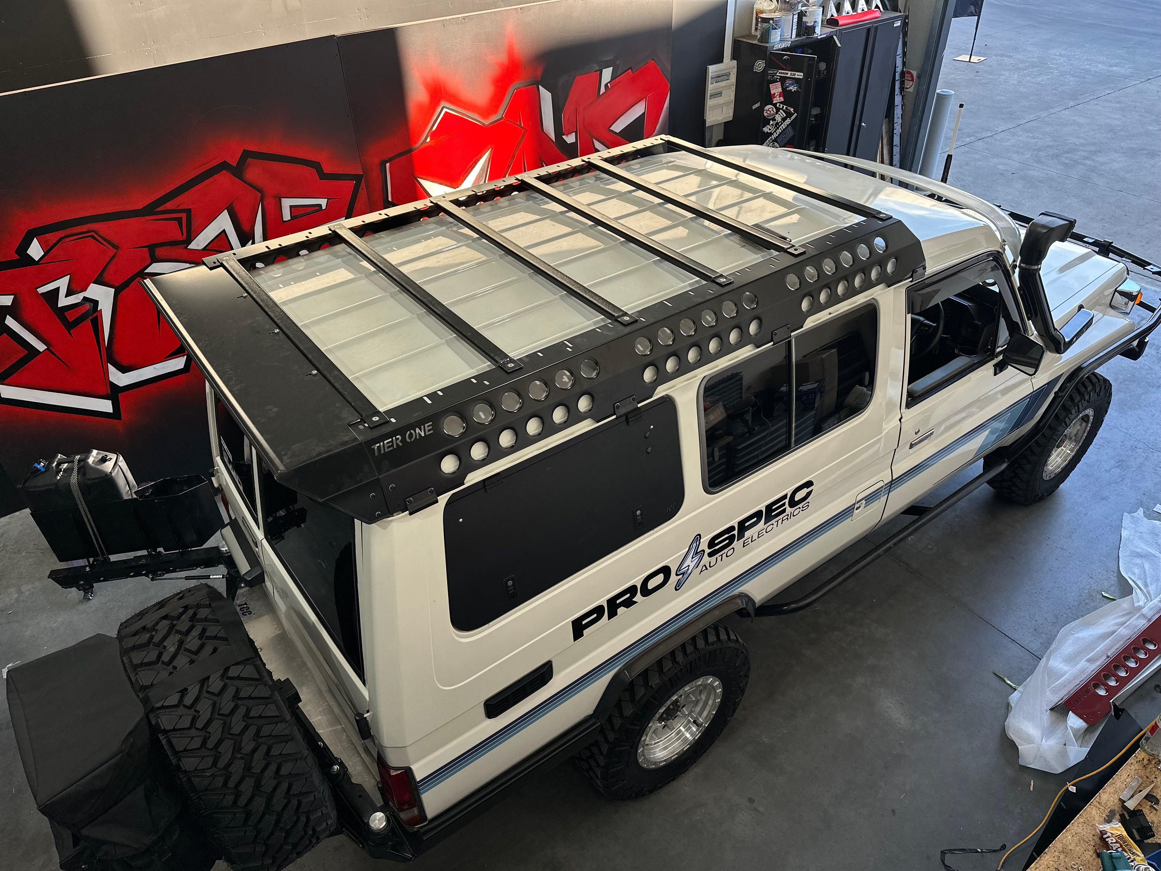 This is an image of a white 4x4 vehicle with Tier One Metalworks Roof Racks & Rails installed in a workshop.