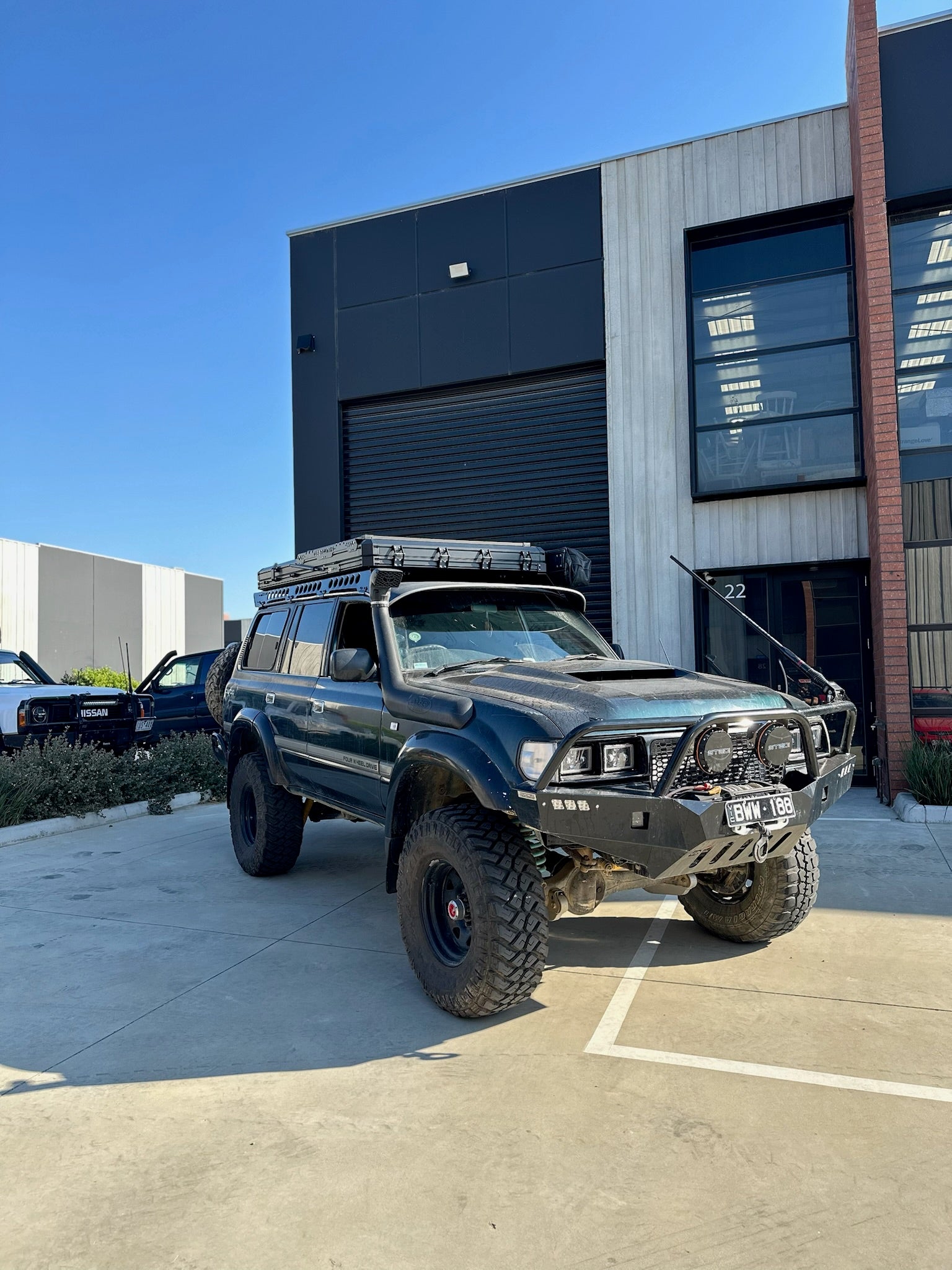 This is an image of a black Toyota Land Cruiser 4WD fitted with Tier One Metalworks roof racks and front bull bar parked outside a workshop