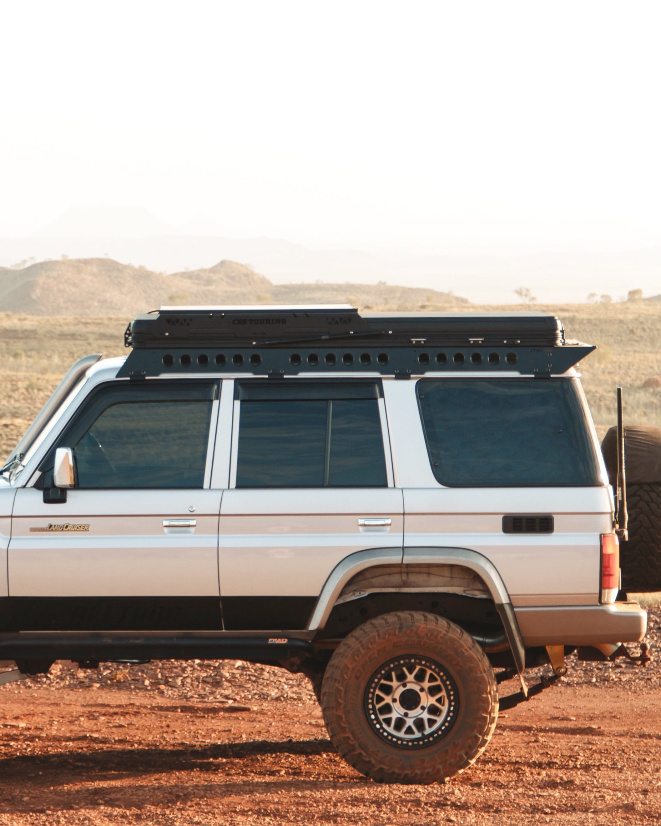 This is an image of the side profile of a Toyota Landcruiser 76 Series driving through outback Australia featuring the Tier One Metalworks Roof Rack Rail Sides and Rear Wing