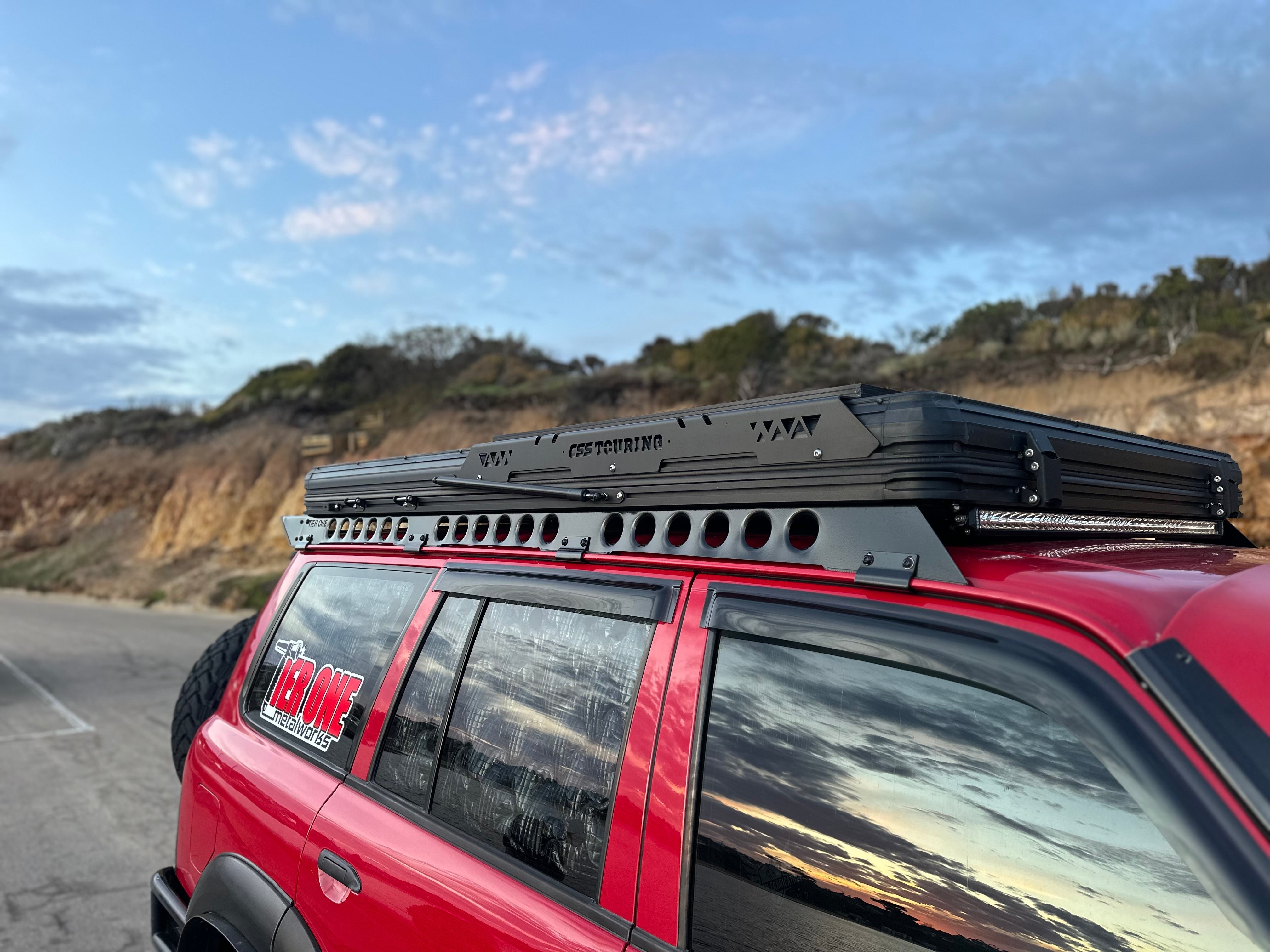 This is an image of a red 4x4 vehicle with Tier One Metalworks roof racks and a CSS Touring rooftop tent at sunset