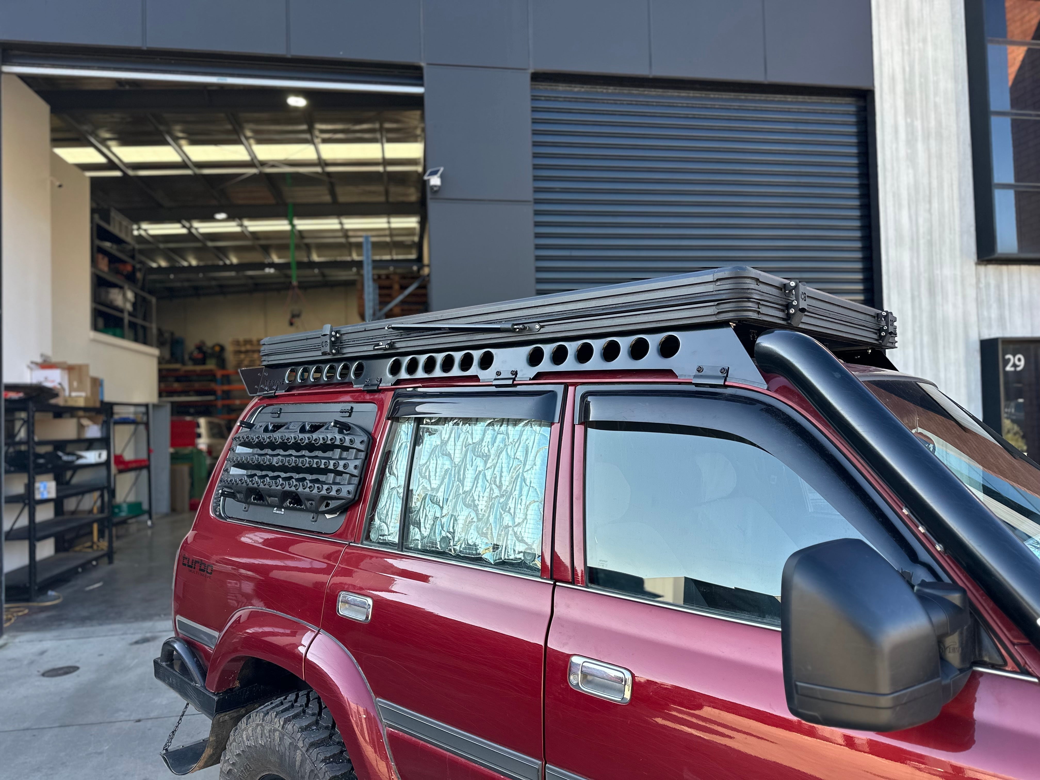 This is an image of a red Toyota LandCruiser 80 series with Tier One Metalworks roof rack and sand tracks mounted on the rear side window