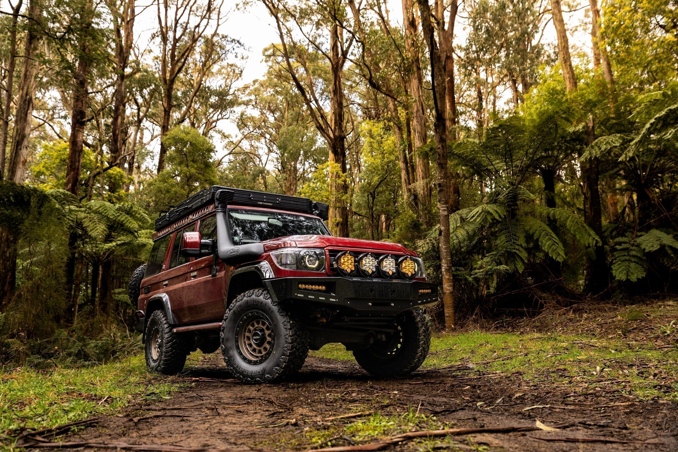 This is an image of a red Toyota Land Cruiser 76 Series in forest with Tier One Metalworks roof rack and snorkel