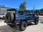 This is an image of a blue Nissan Patrol 4WD with Tier One Metalworks roof racks and rails, off-road tyres and rear spare wheel.