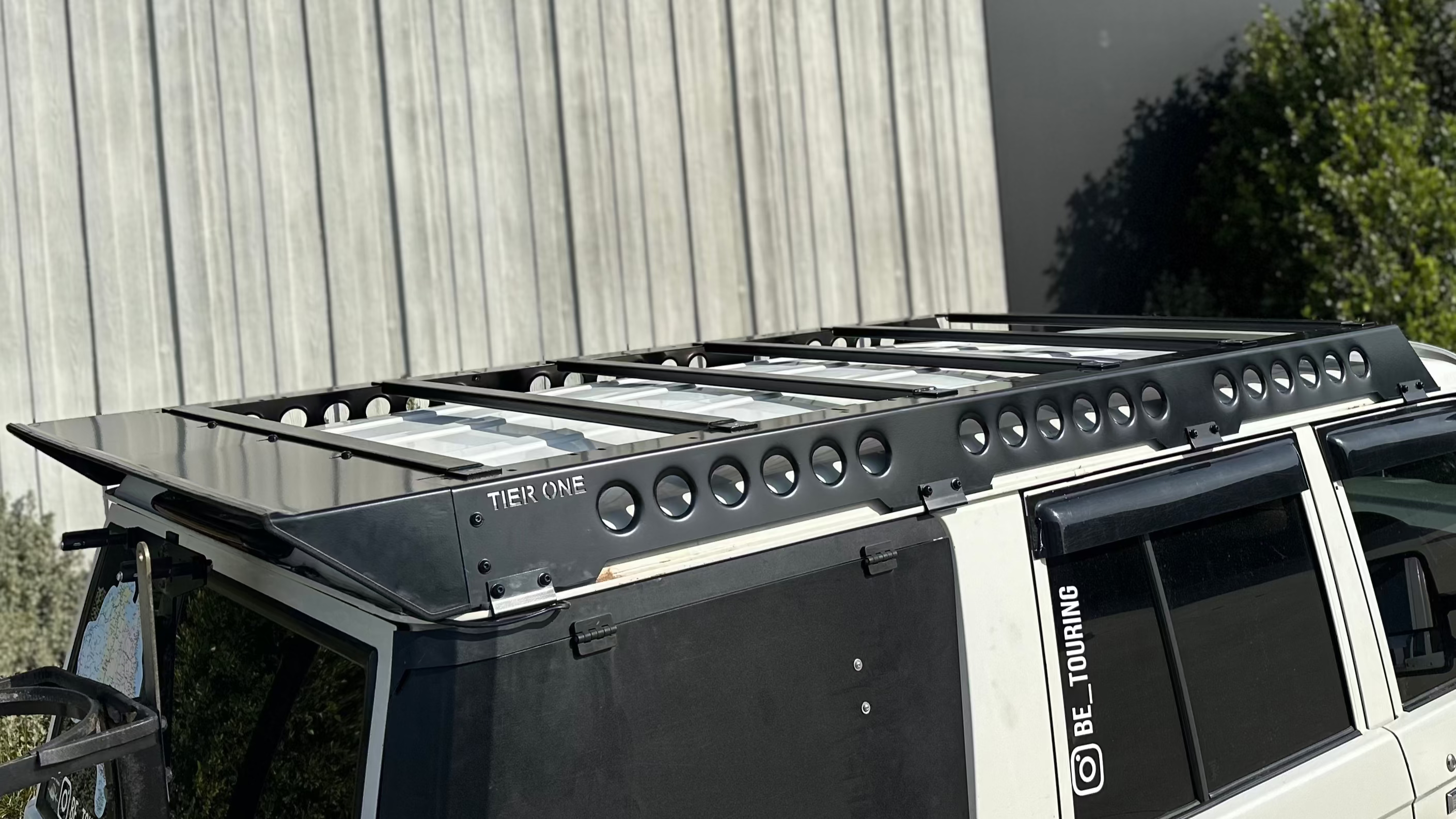 This is an image of a white 4WD fitted with a black Tier One Metalworks roof rack and rails on the vehicle roof