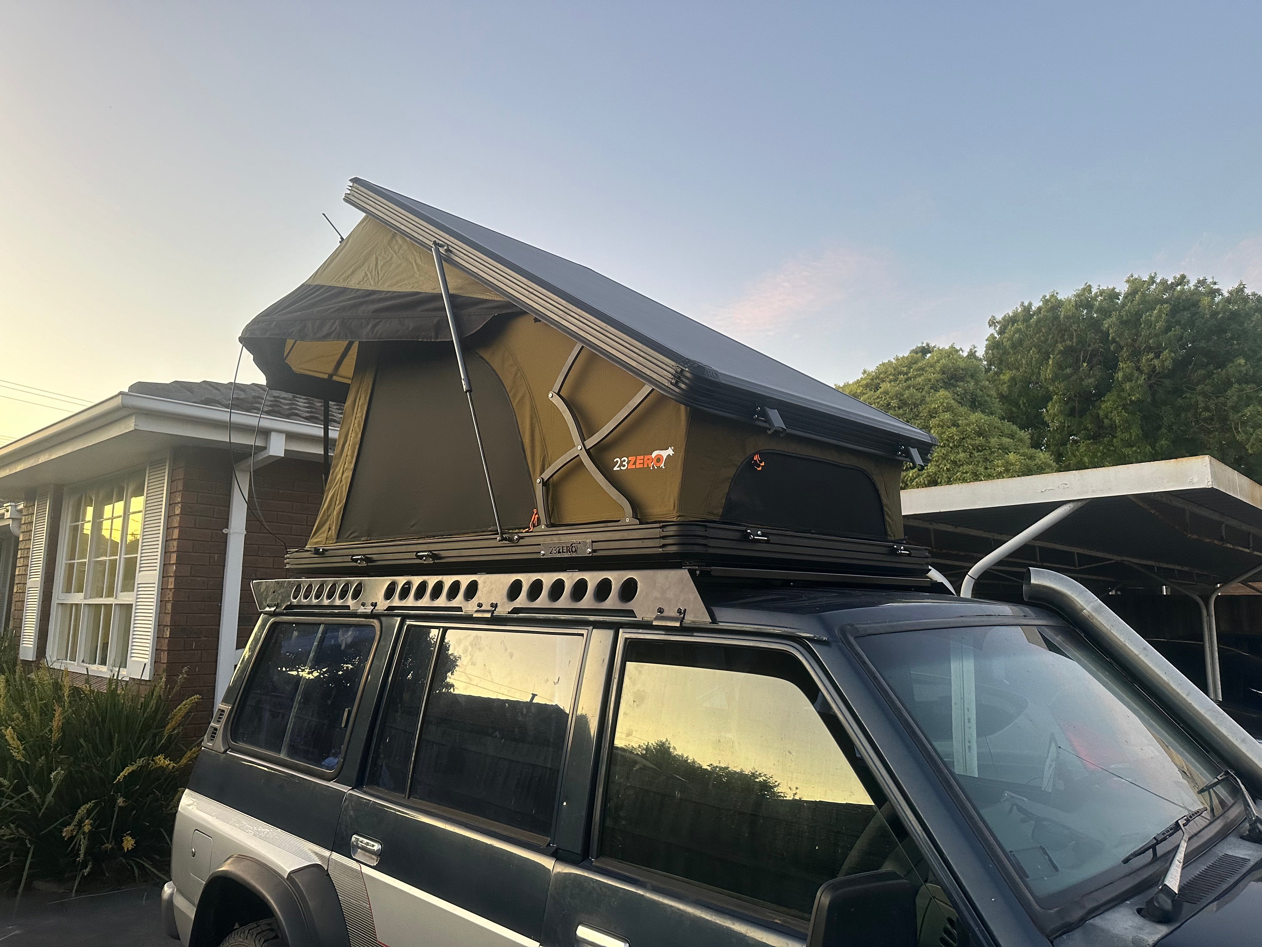This is an image of a black and silver 4WD vehicle with a green 23ZERO rooftop tent mounted on a Tier One Metalworks roof rack