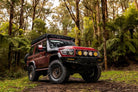 This is an image of a red Toyota Land Cruiser 4WD fitted with Tier One Metalworks roof racks and rails in a forest setting