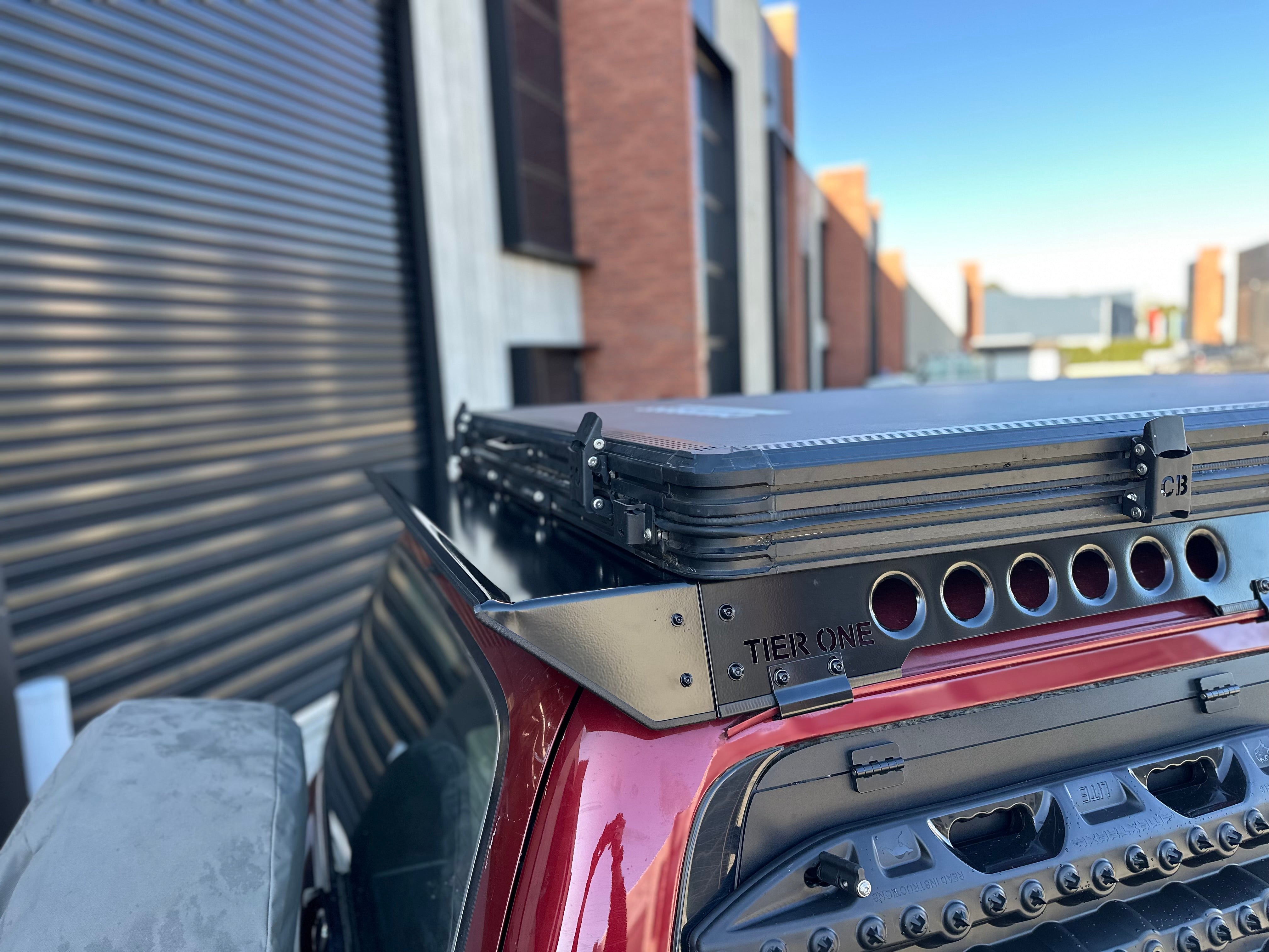 This is an image of a red 4WD with a Tier One Metalworks black roof rack and rails on the vehicle's roof in an industrial setting