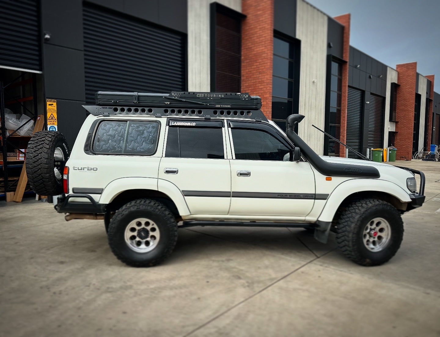 This is an image of a white Toyota Land Cruiser 4WD with Tier One Metalworks roof racks and rails, snorkel, and off-road tyres