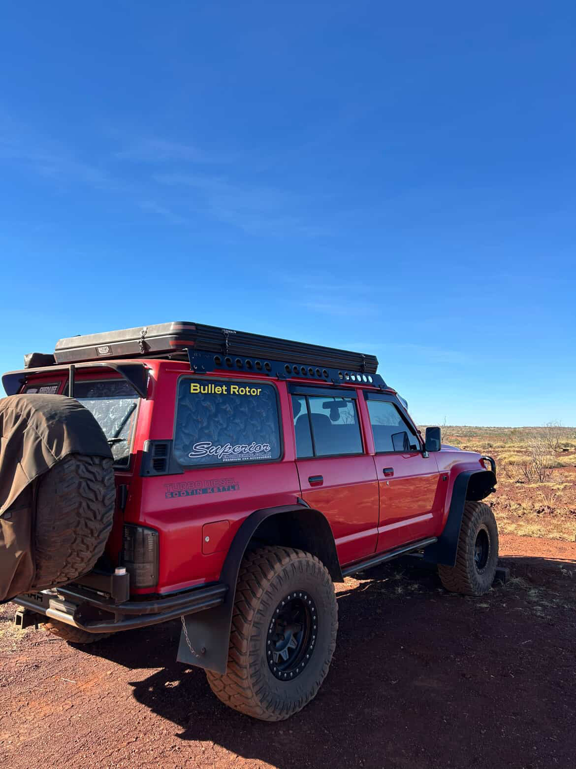 This is an image of a red 4WD Toyota Land Cruiser fitted with a Tier One Metalworks roof rack and rails, off-road tires, set against an Australian outback landscape.