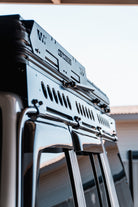 This is an image of a black CSS Touring rooftop tent mounted on a metal roof rack on a 4WD vehicle, promoted by Tier One Metalworks