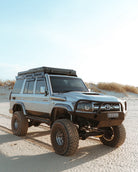 This is an image of a silver Toyota Land Cruiser 4x4 with Tier One Metalworks roof rack and snorkel on sandy terrain