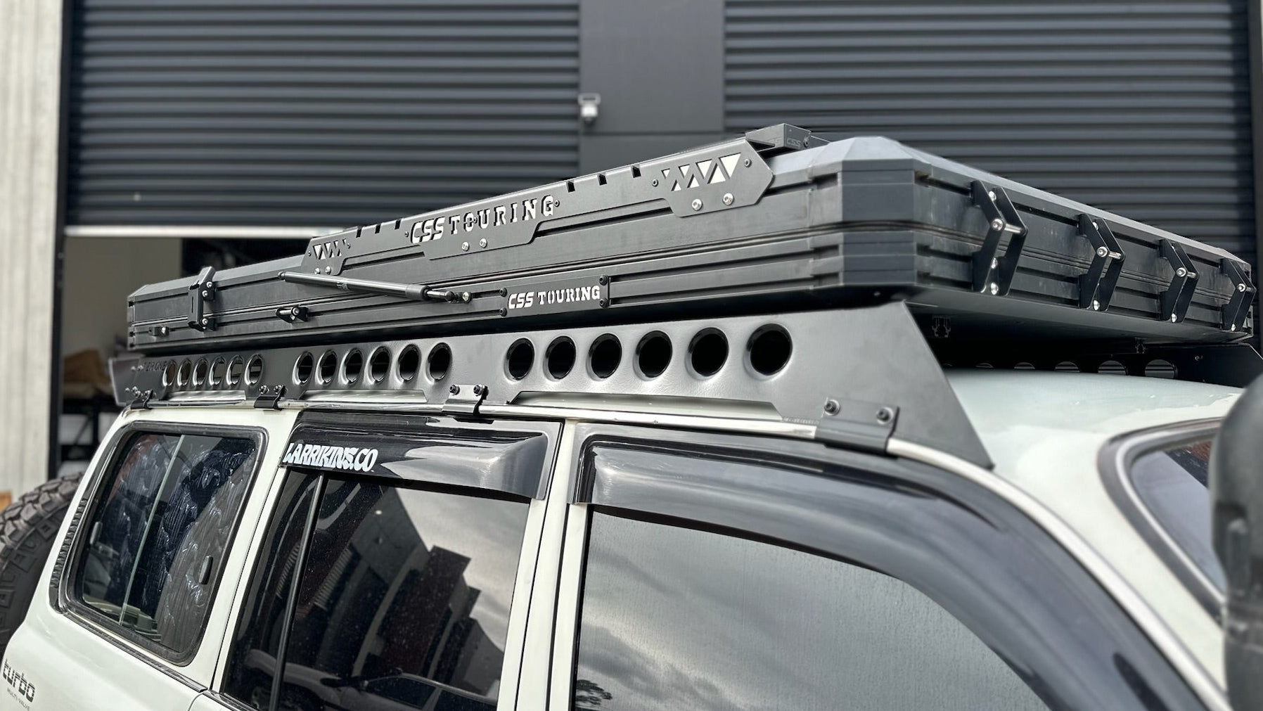 This is an image of a white 4x4 SUV fitted with a CSS Touring rooftop tent on a Tier One Metalworks black roof rack mounted on the vehicle's roof rails