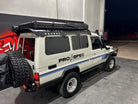 This is an image of a white Toyota Land Cruiser 4WD with Tier One Metalworks roof rack and rails, off-road tyres, and PRO SPEC signage on the side