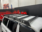 This is an image of a black Tier One Metalworks roof rack mounted on a white Nissan Patrol 4x4 in a workshop