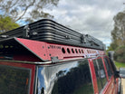 This is an image of a red 4x4 with a Tier One Metalworks black roof rack fitted on top on a rainy day