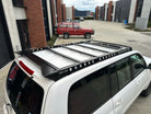 This is an image of a white Toyota 4x4 fitted with a black Tier One Metalworks roof rack in an industrial parking lot