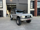 This is an image of a silver Nissan Patrol 4WD fitted with Tier One Metalworks custom roof rack and snorkel, parked outside a modern workshop