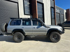 This is an image of a silver Toyota Land Cruiser with Tier One Metalworks roof racks and snorkel, fitted with large offroad tyres
