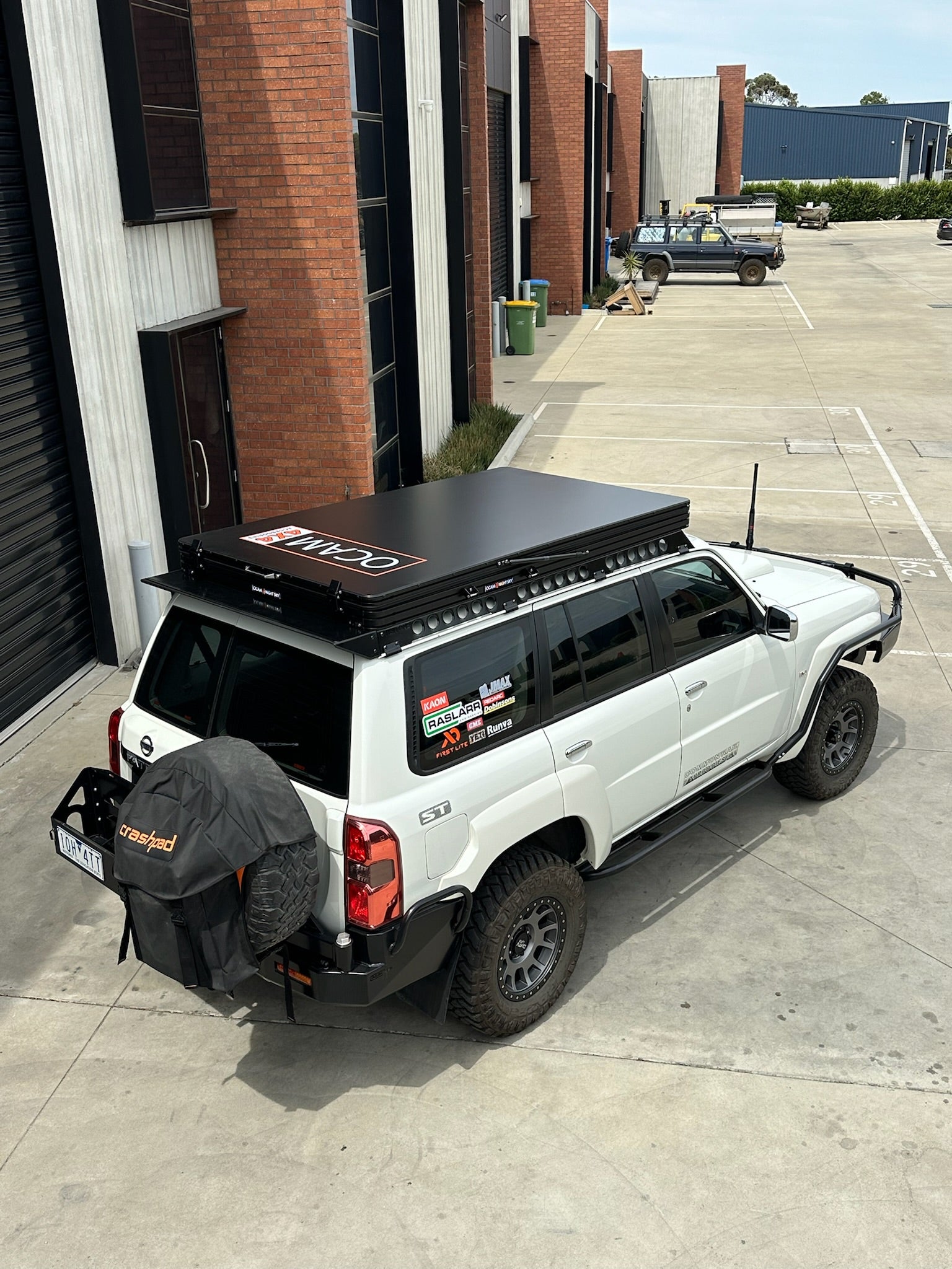 This is an image of a white Nissan Patrol ST with Tier One Metalworks black roof rack and roof top tent in an industrial car park
