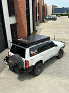 This is an image of a white Nissan Patrol ST with Tier One Metalworks black roof rack and roof top tent in an industrial car park