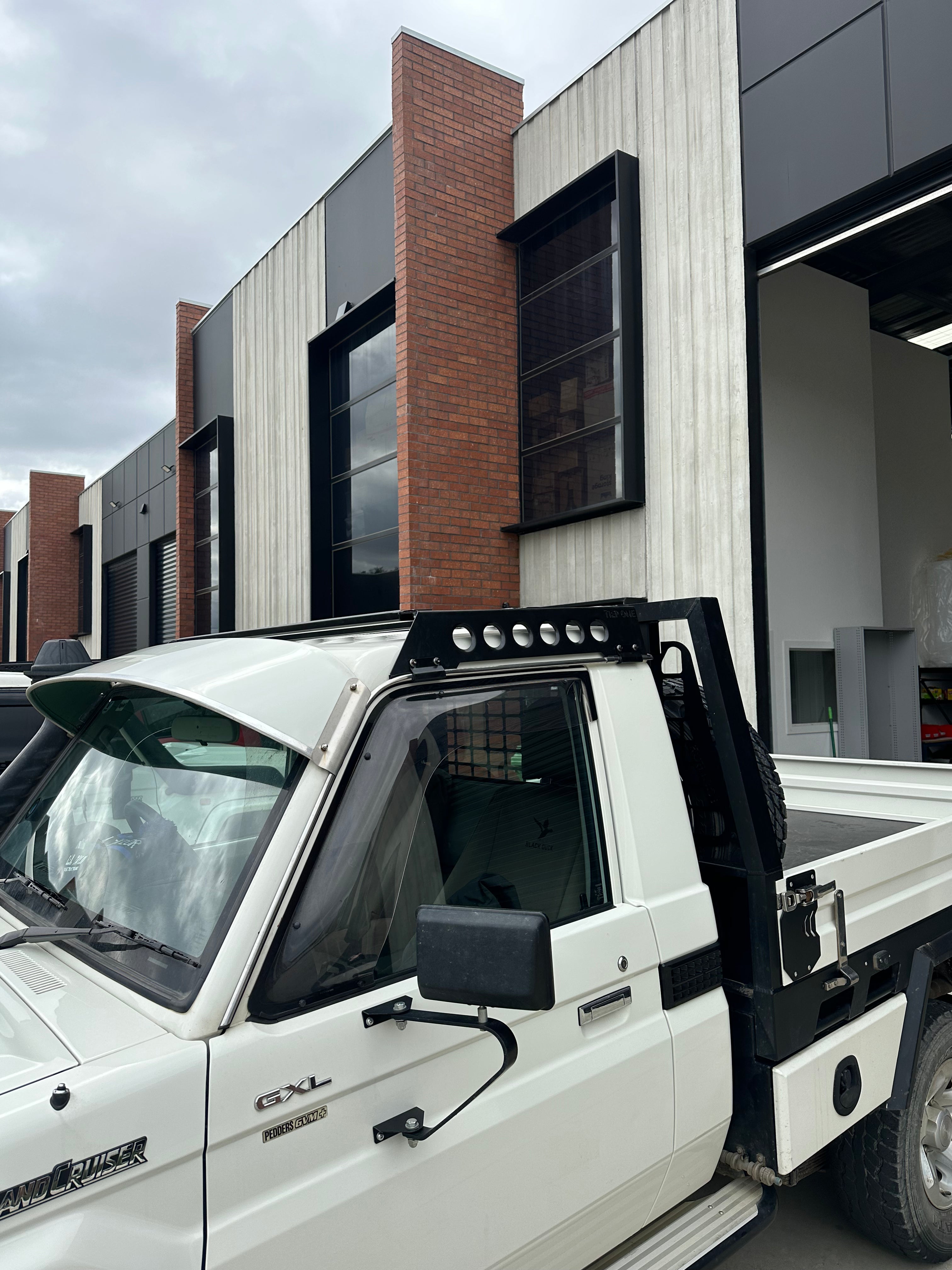 This is an image of a white Toyota Landcruiser 79 Series Single Cab fitted with Tier One Metalworks black 4x4 roof rack in an industrial setting in Melbourne